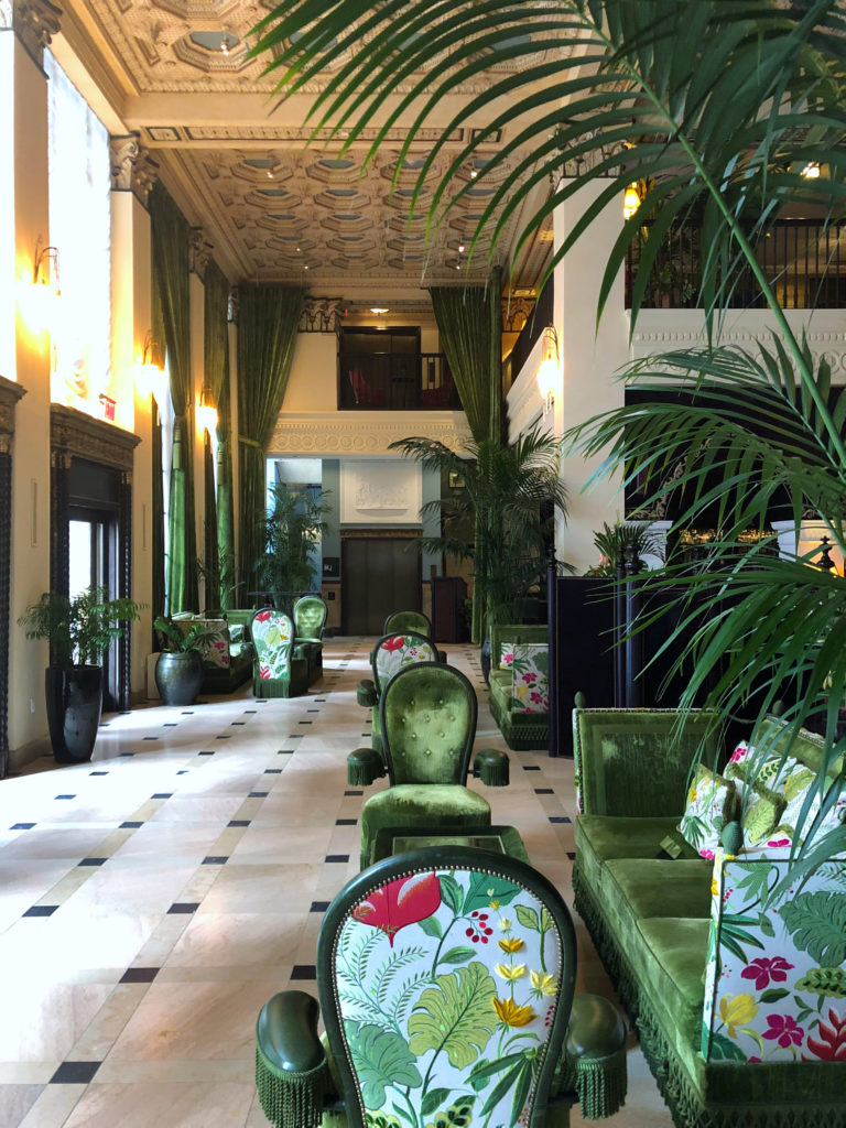 New traditional interior design style - Grand foyer entry with historic neoclassical ceiling over green lounge chairs and botanical plants.