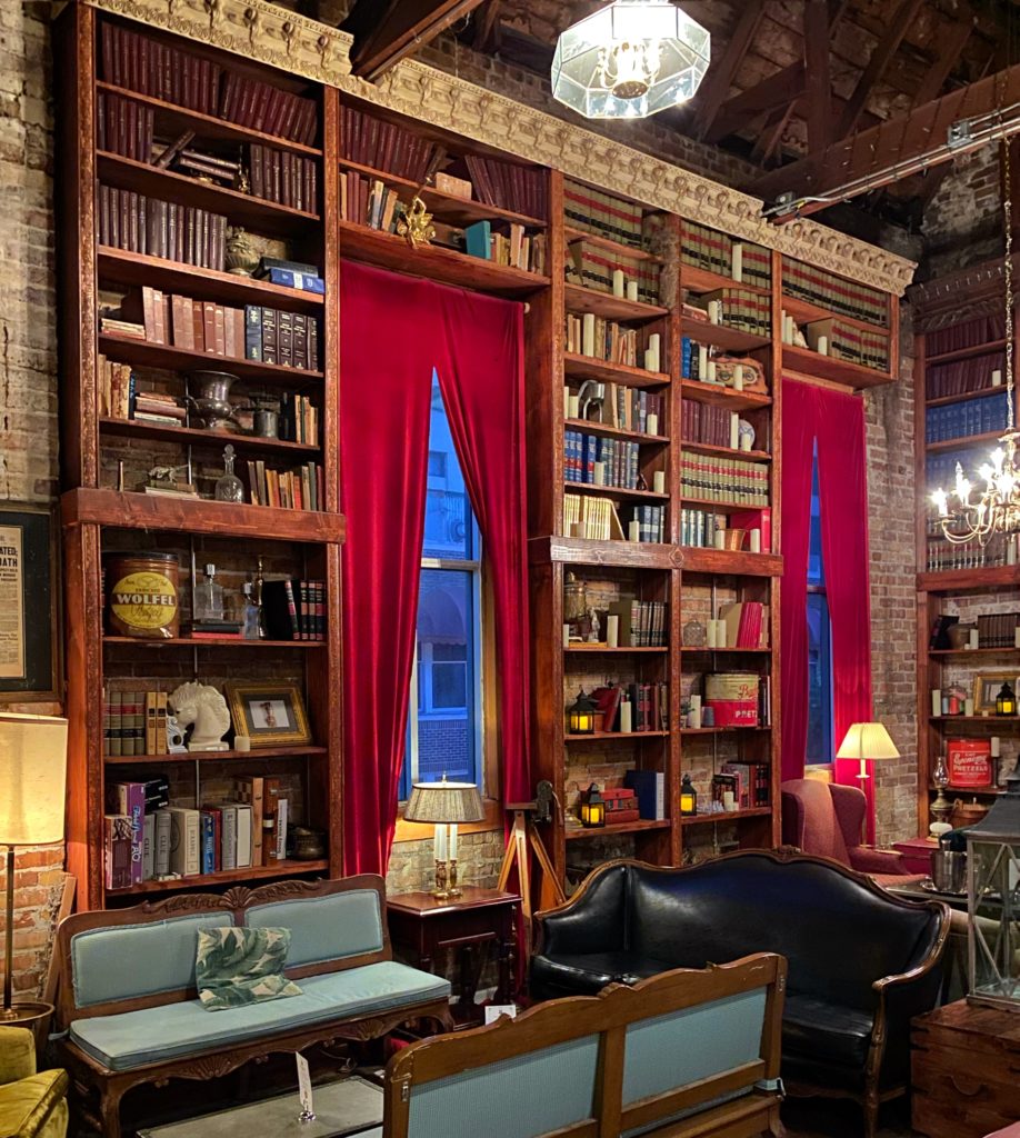 Speakeasy design style - Mathers, Orlando. Large bookshelves, brick wall, red drapery.
