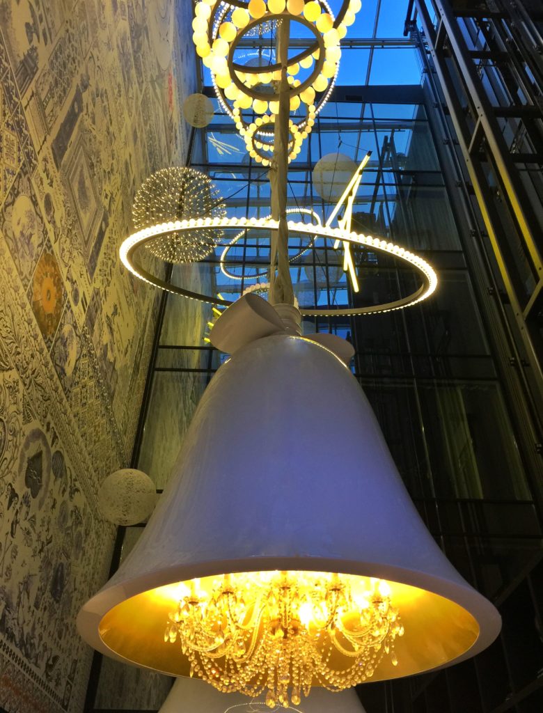 Large glass bell chandeliers and astronomy wallpaper in the atrium at the Andaz hotel in Amsterdam expressing whimsical interior design style.