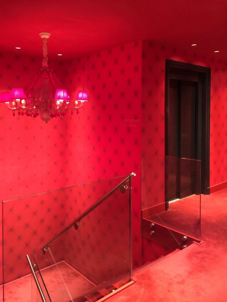 Sultry red room with scarlet chandelier, wallpaper, and carpet at the Andaz hotel in Amsterdam conveys a whimsical interior design style.