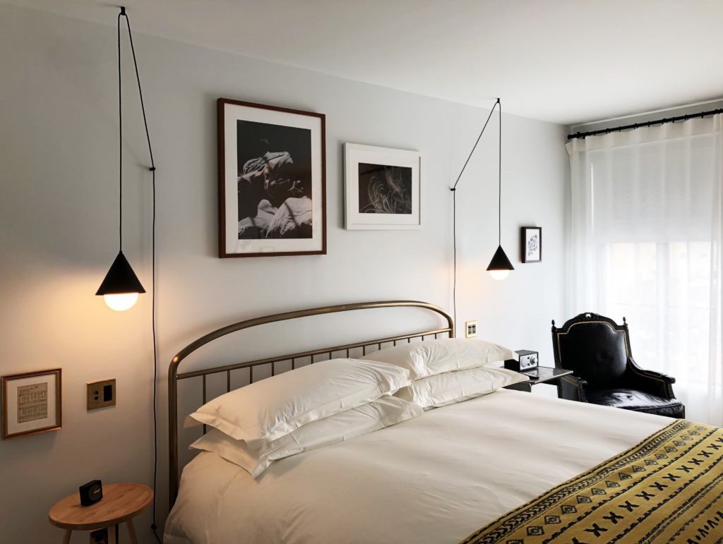 Guest room at the Line Hotel in Washington DC, featuring a brass headboard, hanging pendant lighting, and an art wall.