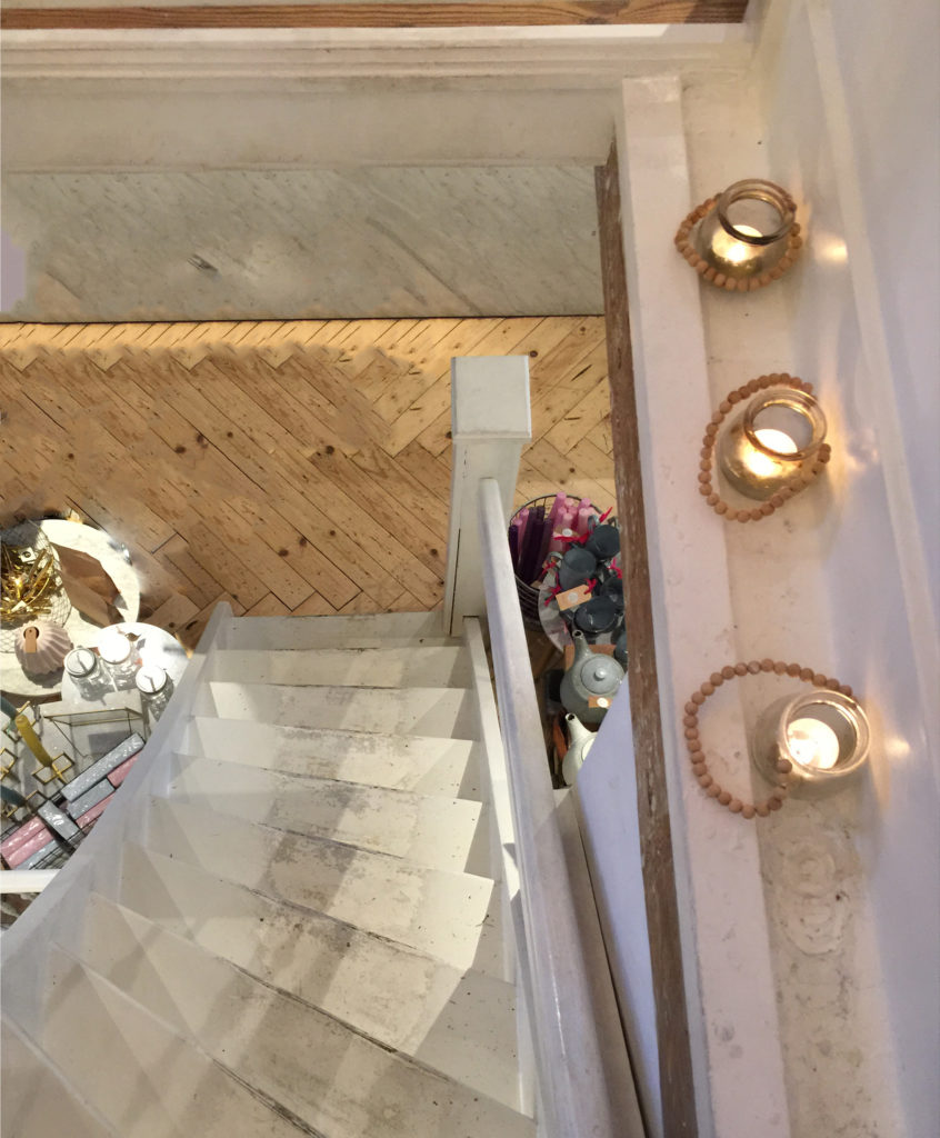 Curved staircase in whitewashed wood leading to the attic mezzanine at Pluk, in Amsterdam - a boho cafe with stylish wares and treats flanked by glowing votive candles.