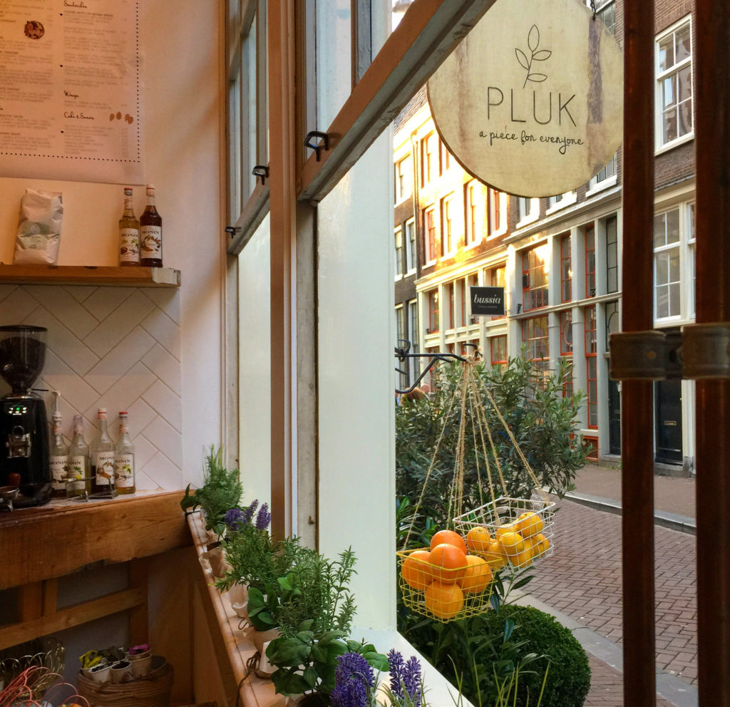 Boho cafe and bakery wtih open window showing signage "Pluk - a piece for everyone" in Amsterdam.
