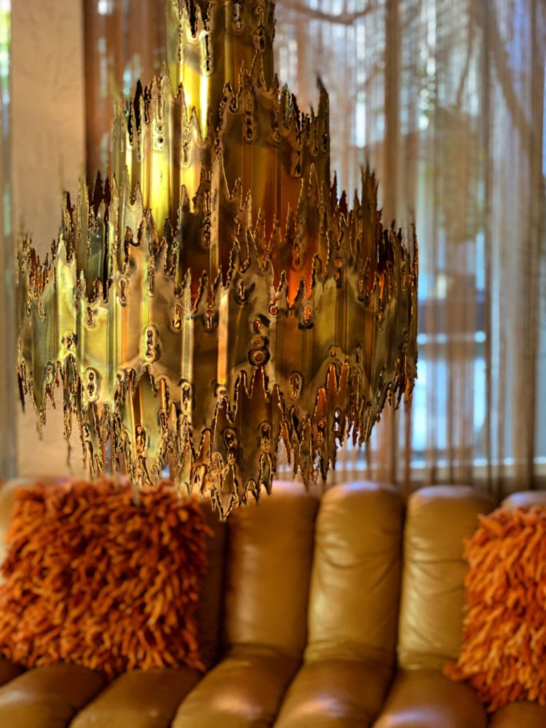 A Bohemian chandelier in matte gold hangs in front of a curved, channel-tufted leather sofa.