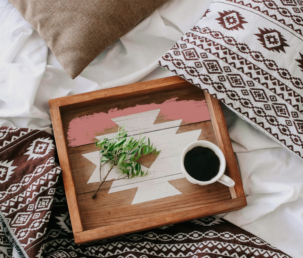 Boho interior design style with wooden tray in bed with patterned textiles.