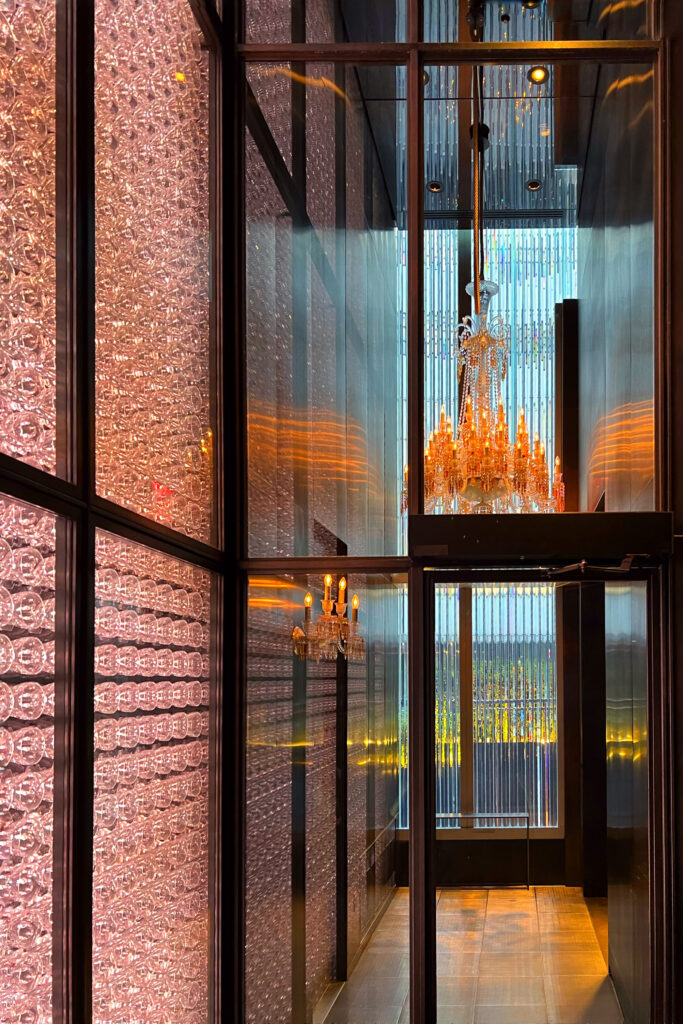 Hanging glass chandelier and undulating wall of backlit glassware at the main entrance to the Baccarat Hotel in New York City.