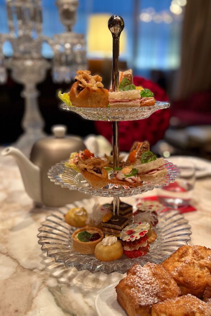 Afternoon tea at the Baccarat Hotel New York, served on a three-tiered crystal tray with elegant finger sandwiches, pastries, and scones.