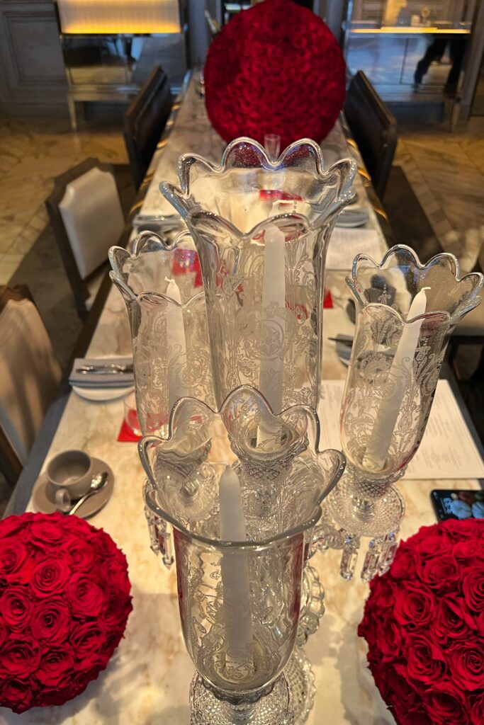 Crystal candlesticks with etched glass detail and red rose centerpieces on a marble table at Baccarat Hotel New York afternoon tea, blending French luxury with interior design elegance.”