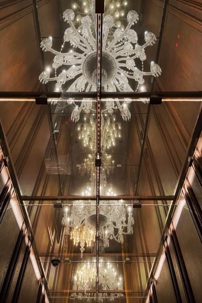 Three glowing glass chandeliers hang overhead at the lobby entrance to the Baccarat Hotel in New York City.