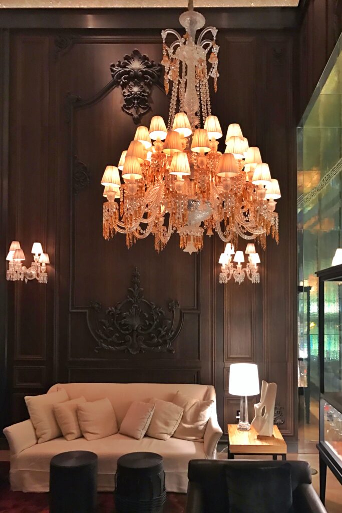 Dark and moody wood paneling contrasts the glowing glass chandelier at the Baccarat Hotel in New York City.