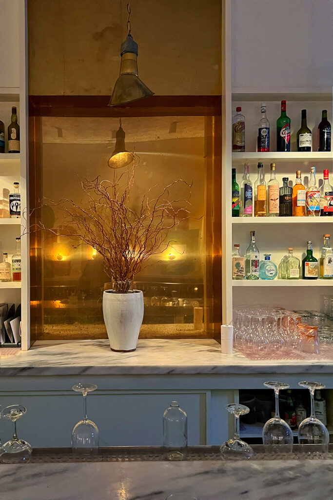 The large gold mirror as the botanical backdrop is the focal point, highlighting the bloomcore interior design trend at Il Fiorista restaurant in New York City.