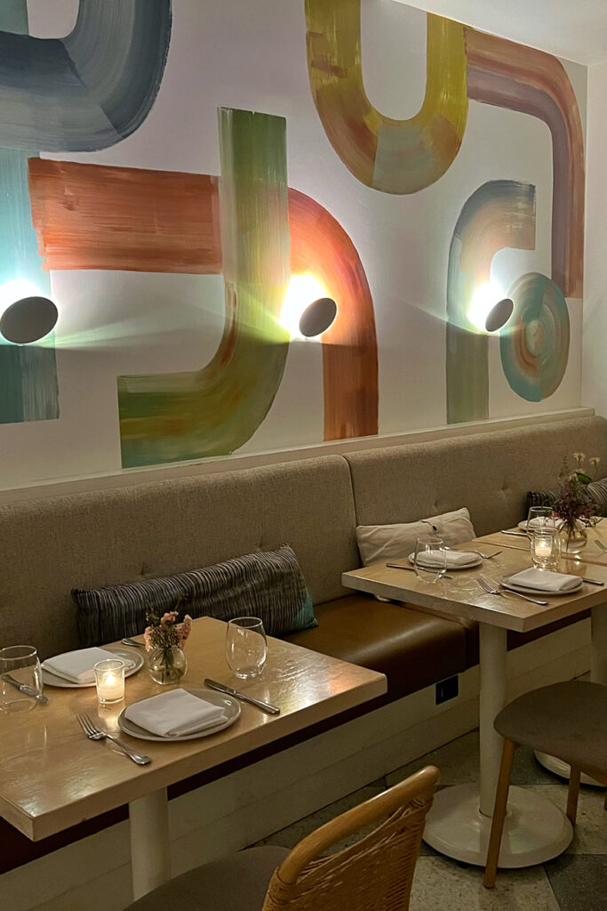 The feature artwork graphic uses bold flourishes of color above the button-tufted banquette. The interior design of Il Fiorista is neutral with accents in the artwork and the bloomcore floral touches on the tables.