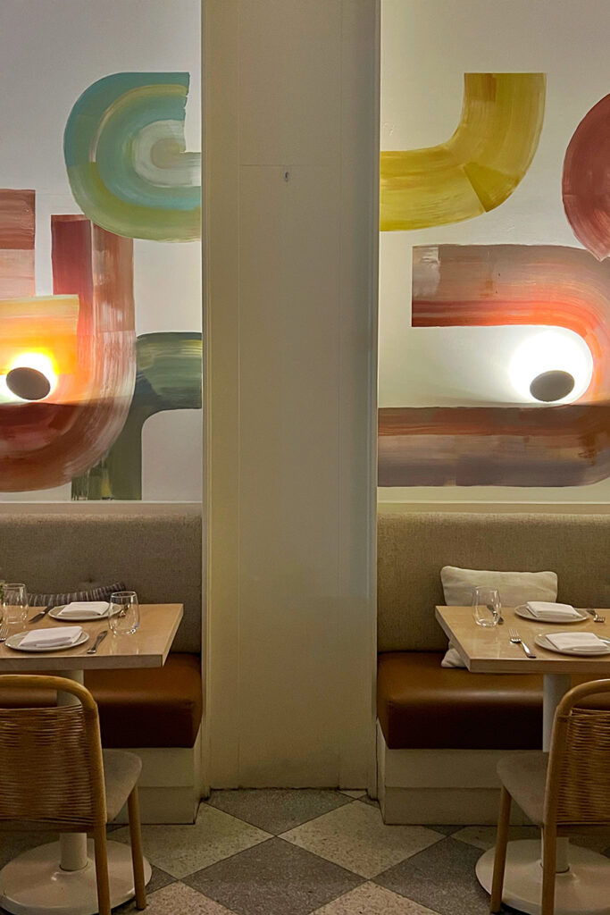 The bold flourish of the artwork wall graphic straddles the large architectural column and banquette seating at Il Fiorista restaurant in New York City.