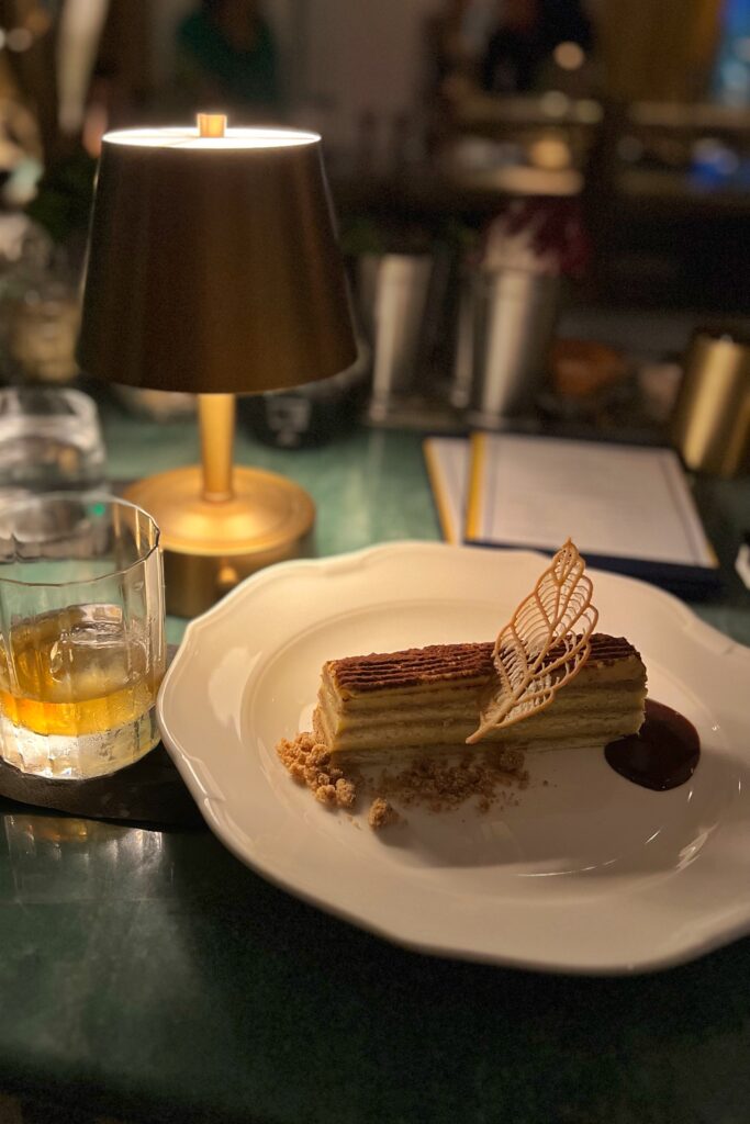 A glass of bourbon and a desert served next to a table light at the Sunset Bar in the lobby of the Georgian Hotel in Santa Monica.