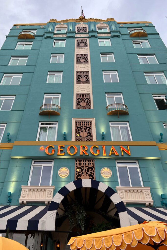 Upward looking view of the turquoise facade of the Georgian Hotel in Santa Monica with lit marquee signage.
