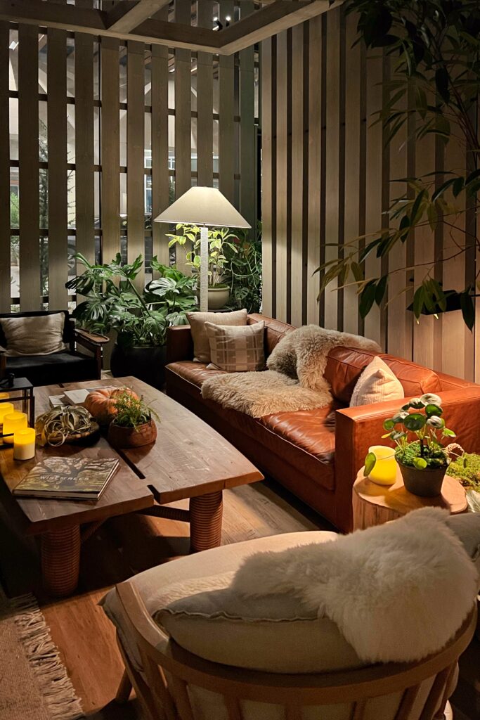 Warm lounge seating at 1 Hotel Nashville lobby with leather sofa, sheepskin throws, wood table, and lush greenery for a nature-inspired retreat.
