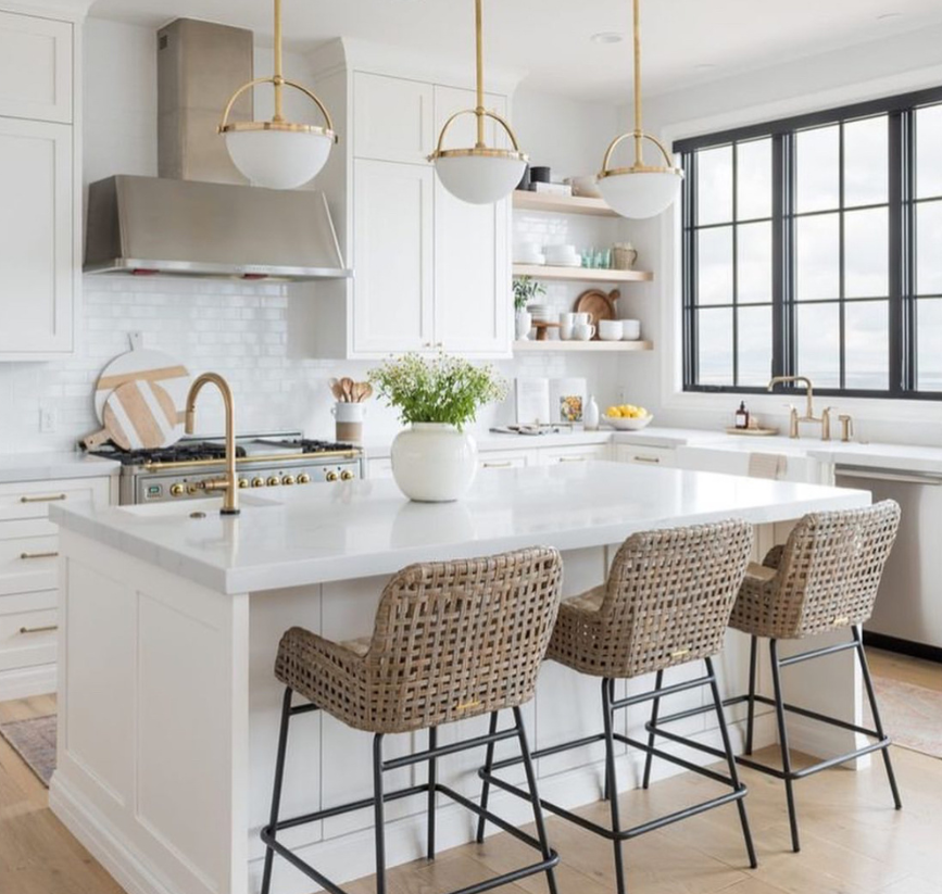 This is a beautiful white, modern kitchen interior showing white cabinets, a white island, and rattan barstools.