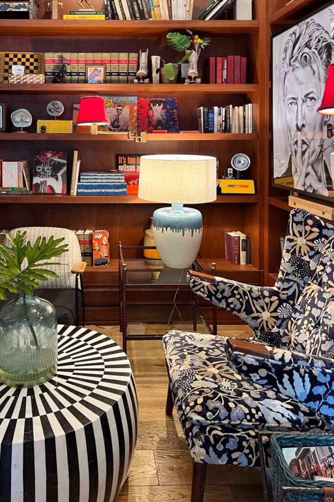 Colorful eclectic hotel lounge design with mid-century chairs, bold patterned textiles, black-and-white striped coffee table, and curated art display