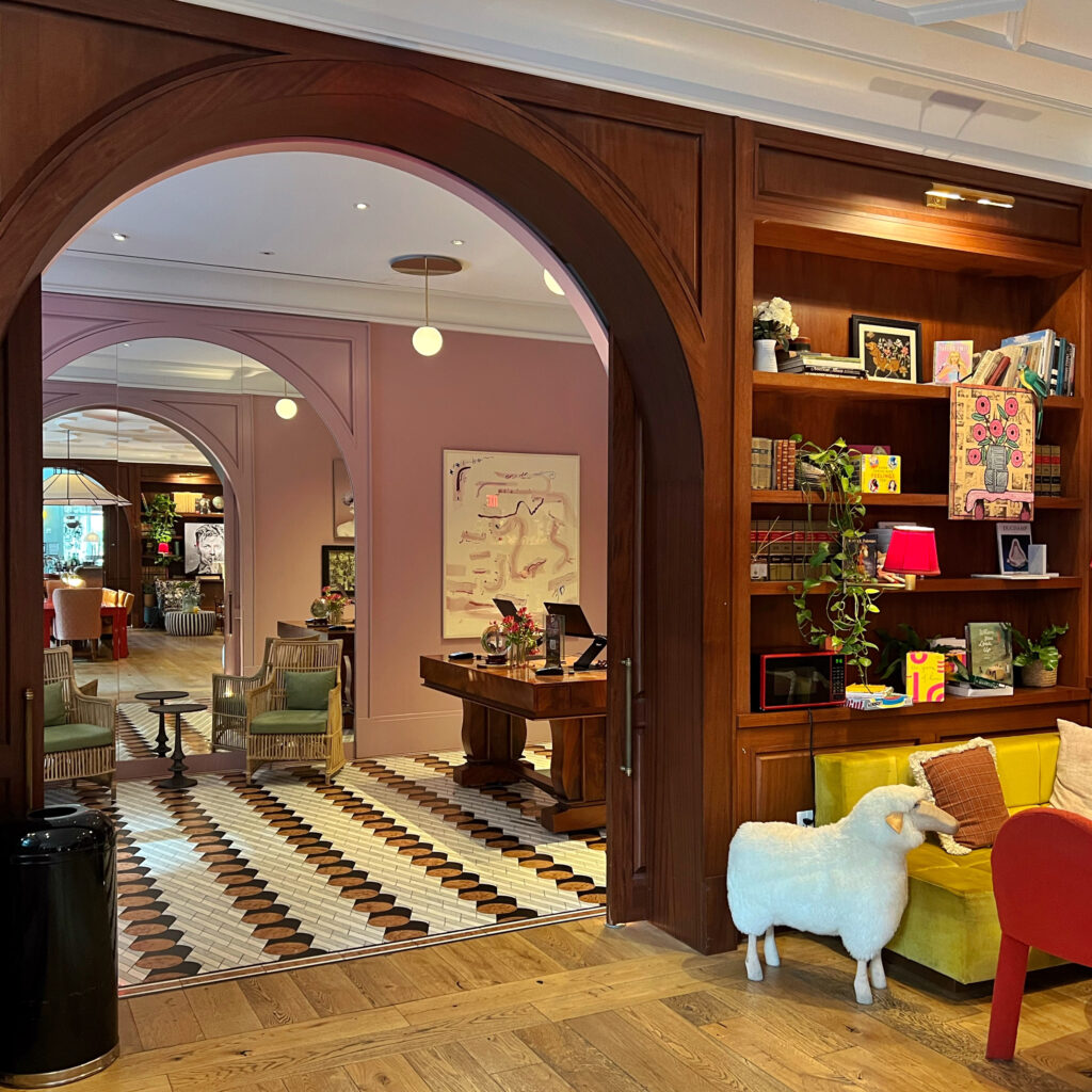Lobby area at Virgin Hotel New Orleans with arched wood doorway, patterned tile floor, and eclectic decor including a plush sheep sculpture