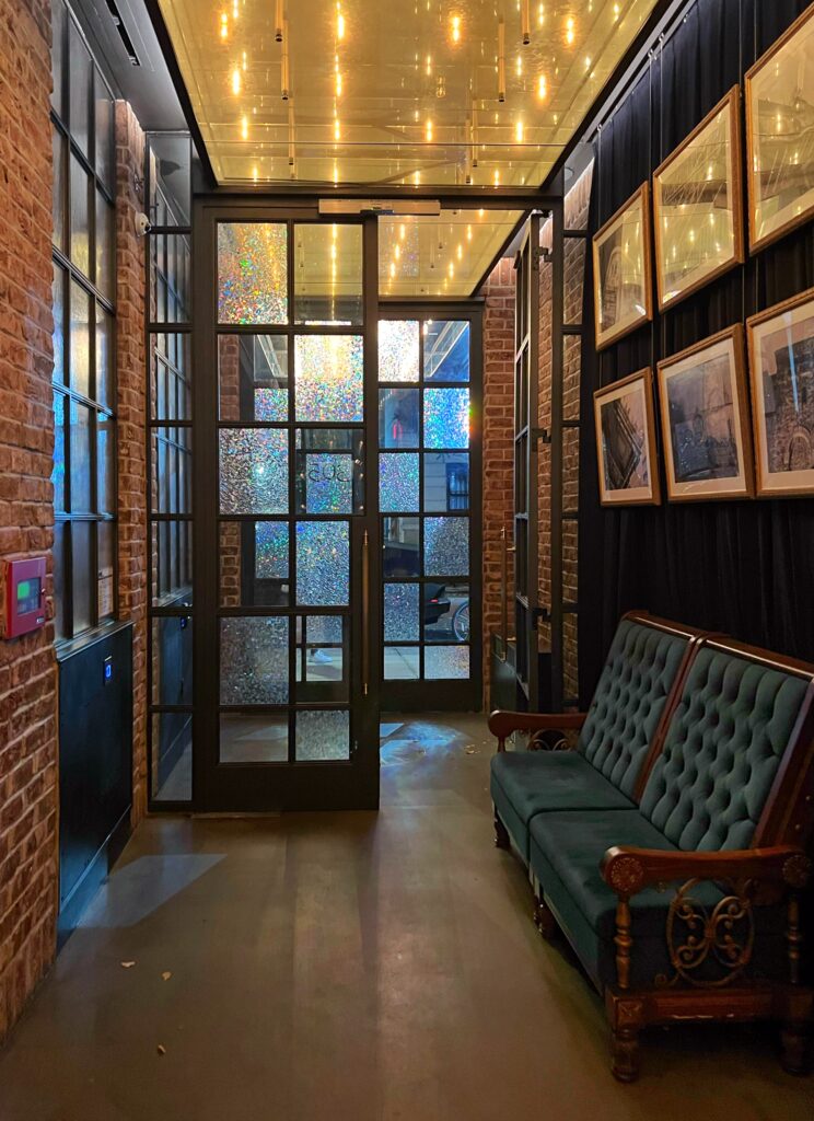 Main entry at the Civilian Hotel with glass doors and an upholstered sofa inside one of New York City's most aesthetic spaces.