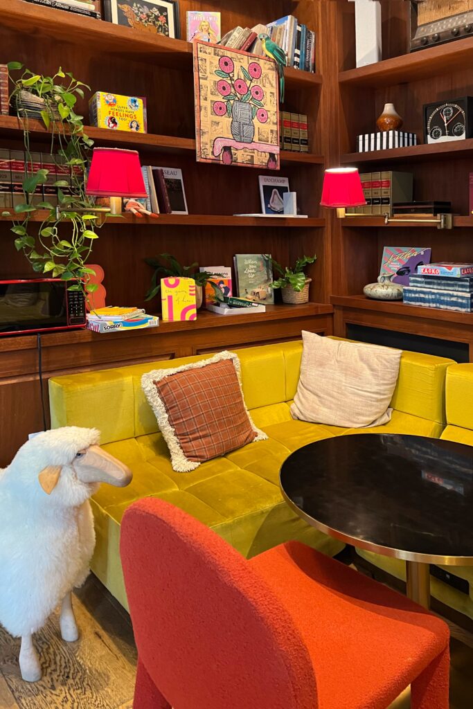 Cozy seating nook at Virgin Hotel New Orleans with mustard yellow sofa, playful sheep sculpture, and bookshelves filled with eclectic decor