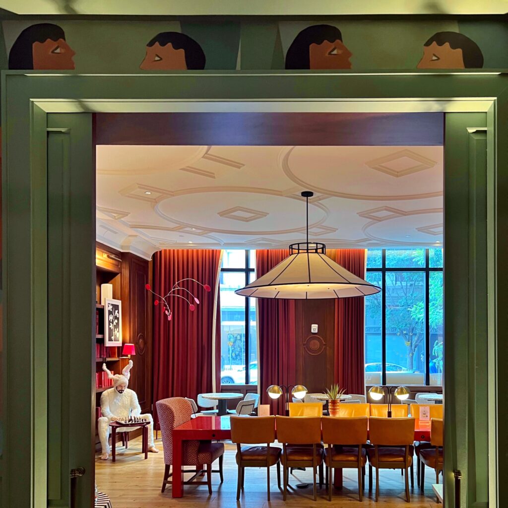Colorful lounge at Virgin Hotel New Orleans with floor-to-ceiling red curtains, large pendant light, and eclectic seating including a whimsical rabbit sculpture
