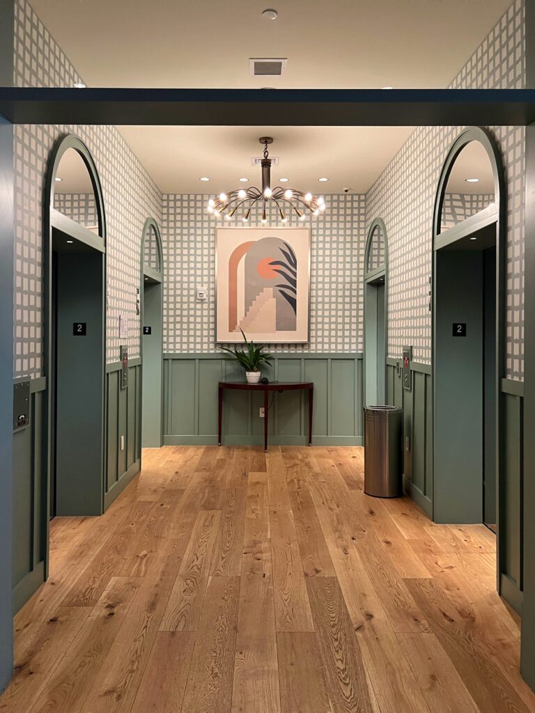 Boutique hotel hallway design featuring sage green wainscoting, checkered wallpaper, abstract wall art, and statement light fixture