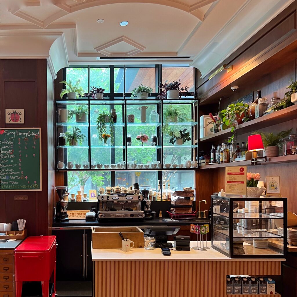 Coffee bar at Virgin Hotel New Orleans with plant-filled shelves in the window, espresso machine, and warm wood finishes