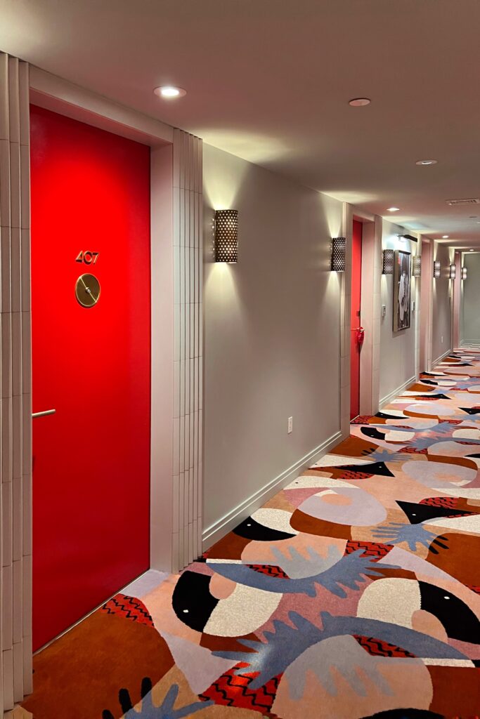 Colorful hallway at Virgin Hotel New Orleans featuring vibrant red doors, modern wall sconces, and abstract multicolor carpet design