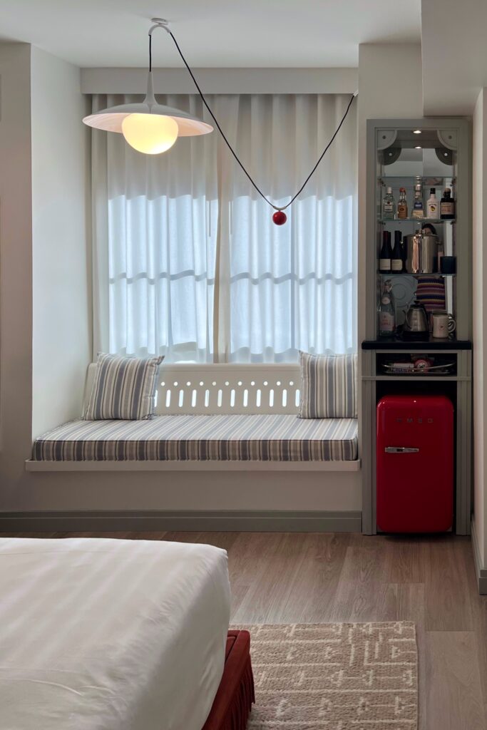 Cozy window seat at Virgin Hotel New Orleans with blue and white striped cushions, modern pendant light, and retro red Smeg refrigerator