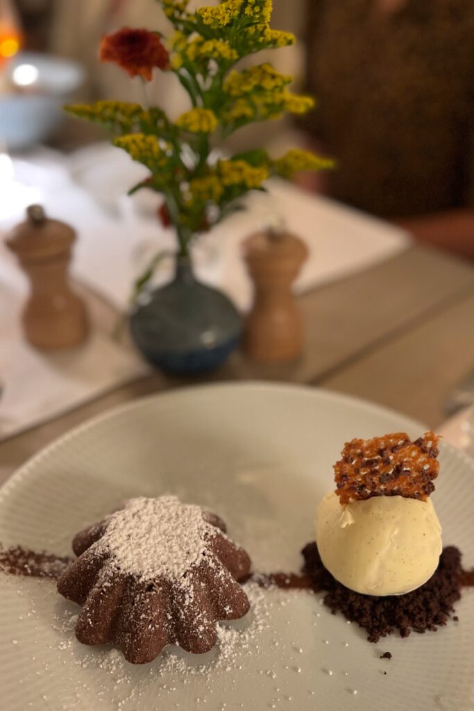 Chocolate cake dessert at Drusie & Darr inside the Hermitage Hotel in Nashville, dusted with powdered sugar and paired with vanilla ice cream on cocoa crumble, topped with a caramelized crisp — a refined culinary presentation within a design-forward dining setting.