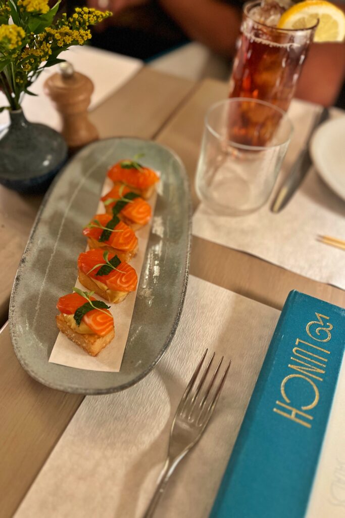Crispy sushi appetizer at Drusie & Darr inside the Hermitage Hotel in Nashville, featuring golden crispy rice topped with fresh tuna and herbs, plated on a ceramic dish beside contemporary place settings — a culinary highlight within the restaurant’s refined interior design.