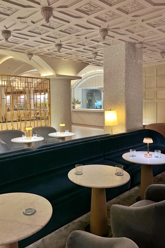 Restaurant banquette lounge seating at Drusie & Darr inside the Hermitage Hotel in Nashville, featuring curved velvet banquettes, marble pedestal tables with brass accent lamps, mosaic-tiled columns, and a coffered ceiling with sculptural detailing — a refined example of Nashville restaurant interior design.