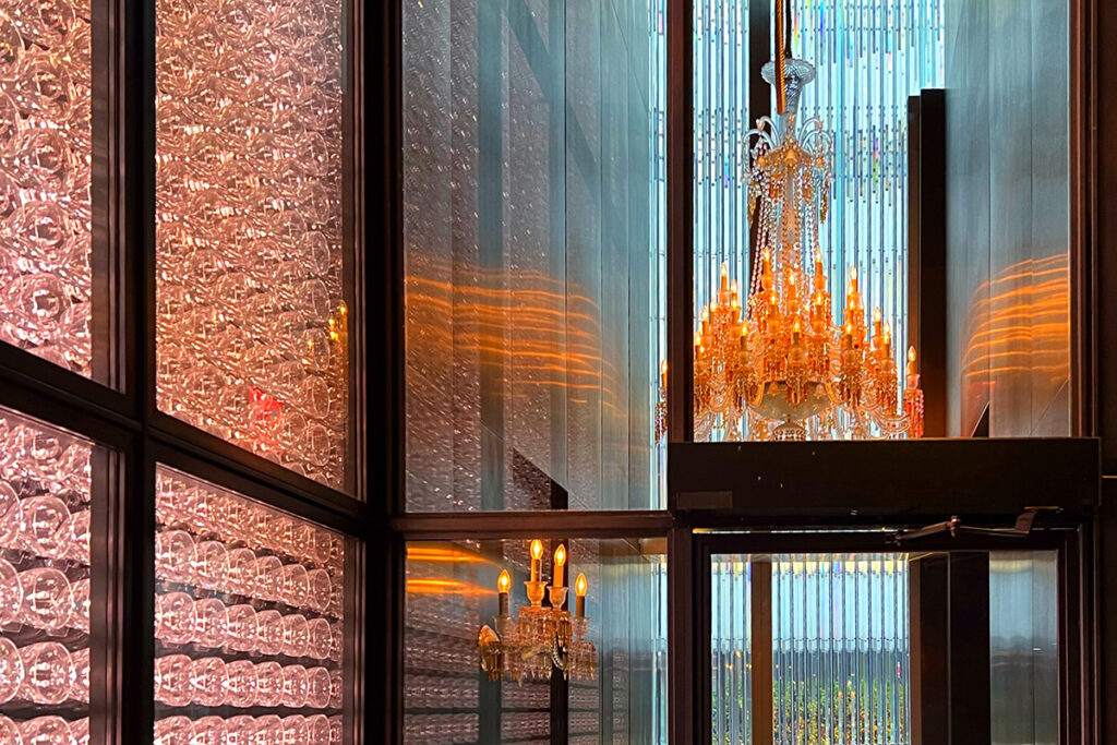 Golden crystal chandelier glowing inside the Baccarat Hotel New York, reflecting against mirrored glass walls — the entry leading to the Grand Salon, for the hotel’s luxurious Afternoon Tea.
