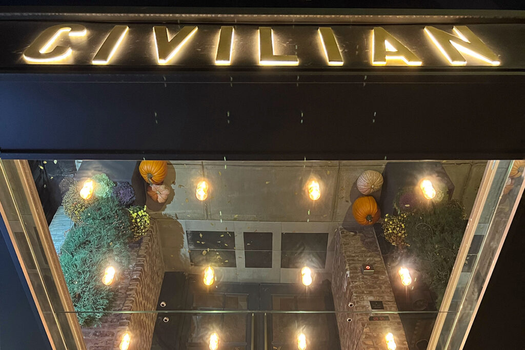 Looking up at the Civilian Hotel entrance in NYC with illuminated marquee lights and glowing “CIVILIAN” sign, a boutique hotel with Broadway-inspired design.