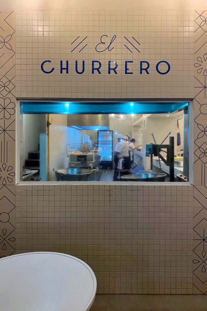 Kitchen view at El Moro Churrería in Mexico City, framed by white tiled walls with blue lettering and geometric patterns where inside they are making churros.