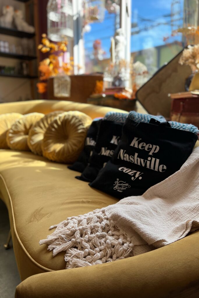 Golden Slipper boutique in Nashville featuring a mustard velvet sofa with 'Keep Nashville Cozy' totes — a stylish stop for shopping in the Nashville Aesthetic Travel Guide.