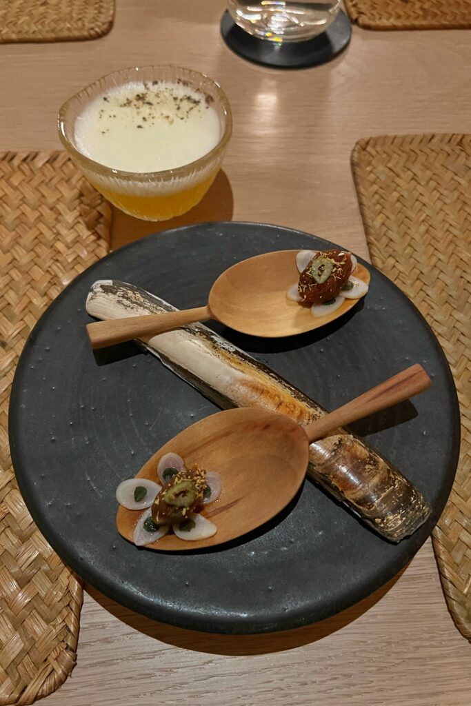 Elegant tasting menu dish at June restaurant in Nashville, served on wooden spoons with cocktail pairing.