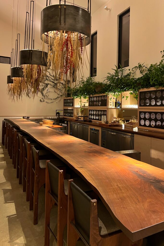 Chef’s counter at June restaurant in Nashville featuring a live-edge wood table, modern lighting with dried botanicals, and intimate fine dining setting.