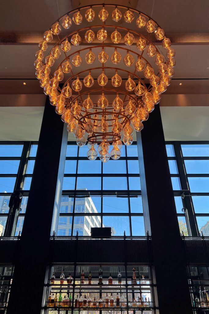 Statement chandelier at the Commons Club inside Virgin Hotel Nashville, glowing against floor-to-ceiling windows with city views — featured in the Nashville Aesthetic Travel Guide.