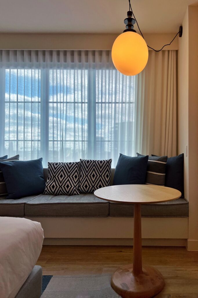 Modern guestroom window seat at Virgin Hotel Nashville with round wood table, graphic black-and-white pillows, and soft natural light filtering through sheer curtains — part of Nashville Aesthetic Travel Guide featuring stylish hotel interiors.