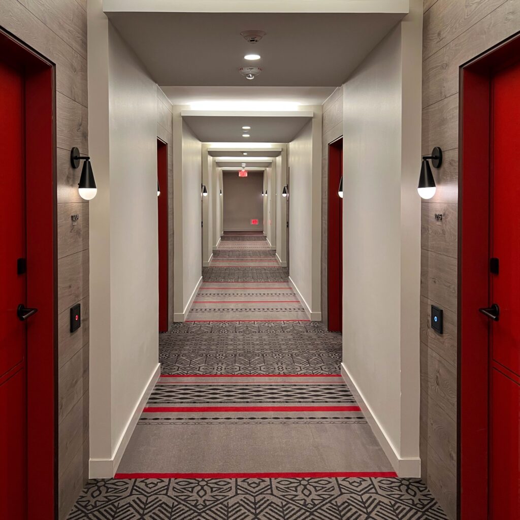 Stylish hallway at Virgin Hotel Nashville featuring bold red doors, patterned carpet, and modern black sconces — Nashville Aesthetic Travel Guide.