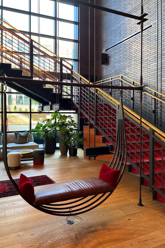Virgin Hotel Nashville lobby featuring a modern leather swing with red pillows, bold red staircase, and industrial-chic design — part of the Nashville Aesthetic Travel Guide.