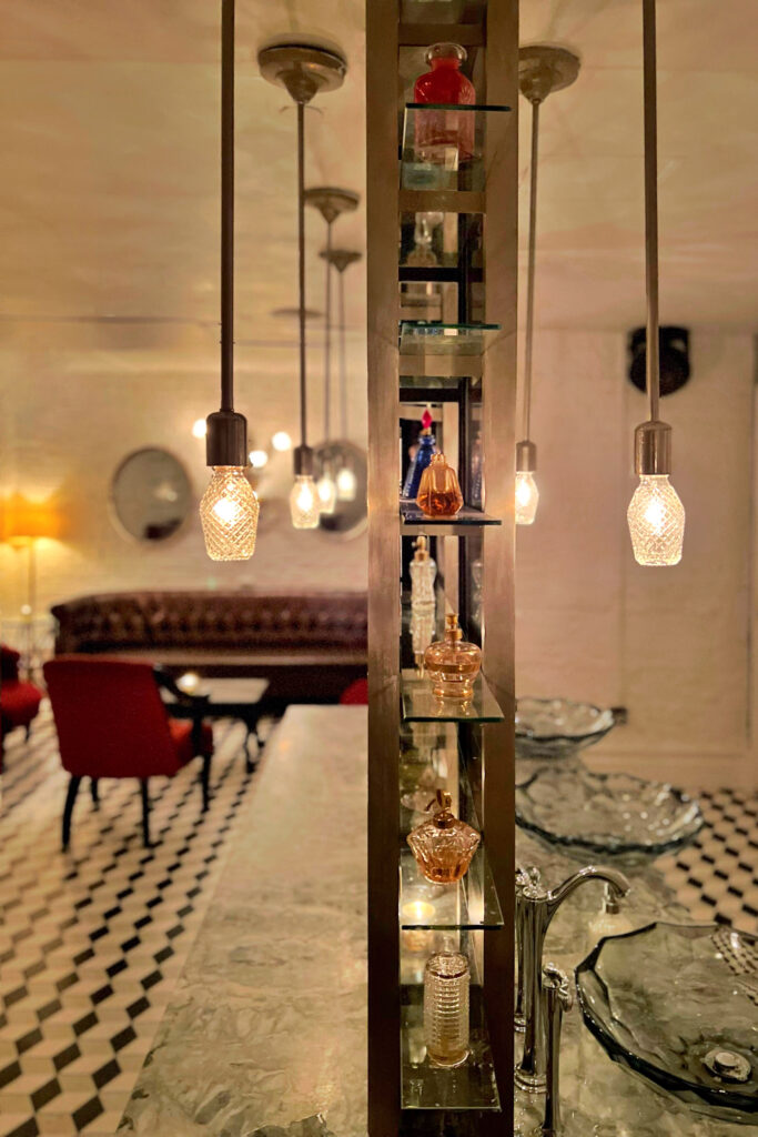Perfume bar inside the women’s lounge at Beauty & Essex NYC, featuring vintage glass perfume bottles, glowing pendant lights, and marble countertops in a glamorous speakeasy design.