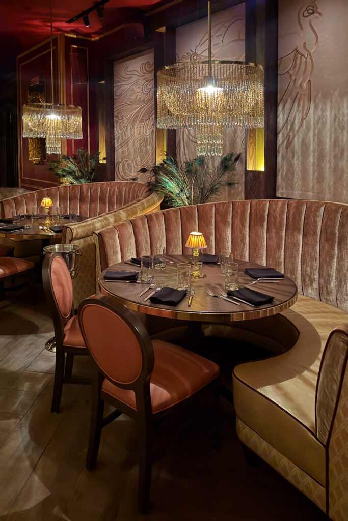 Beauty & Essex restaurant interior with Art Deco design, velvet banquettes, crystal chandeliers, and warm golden lighting creating a speakeasy-style atmosphere.