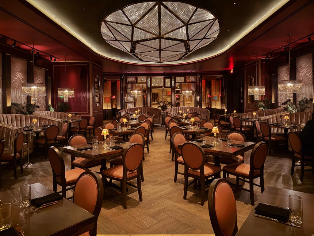 Beauty & Essex restaurant interior featuring velvet banquettes, crystal chandeliers, and warm moody lighting in a luxurious Art Deco speakeasy design.