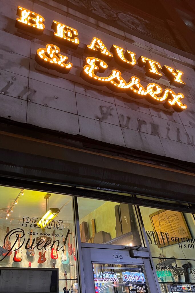 Exterior of Beauty & Essex with illuminated marquee lighting and pawn shop storefront concealing a hidden speakeasy entrance in New York City.