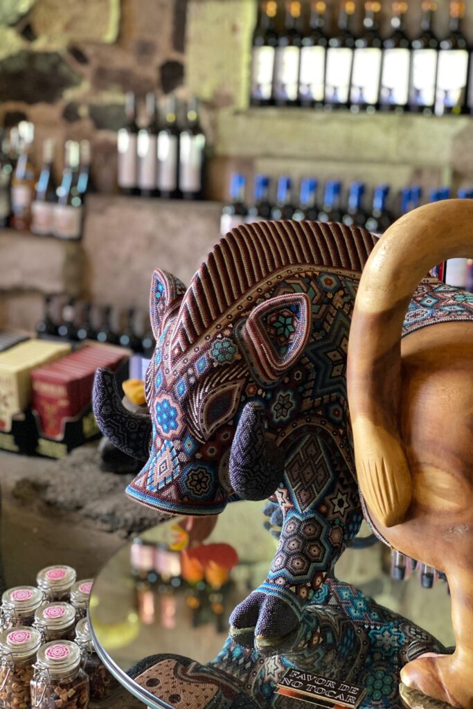 Close-up of a handcrafted Huichol beaded sculpture displayed at Los Limosneros restaurant in Mexico City’s Centro Histórico, set against a backdrop of wine bottles and volcanic stone walls. The intricate beadwork in blue and terracotta hues reflects indigenous Mexican artistry and the design-forward ethos of one of Mexico City’s most beautiful dining spaces.