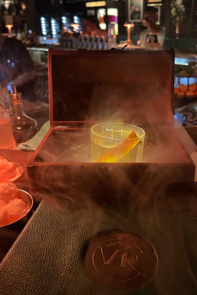 Smoked Old Fashioned cocktail at The Vine Room speakeasy in Naples, Florida, served in a smoky wooden box with a glowing amber hue and citrus twist — an elegant, theatrical presentation that captures the bar’s moody bar aesthetic.