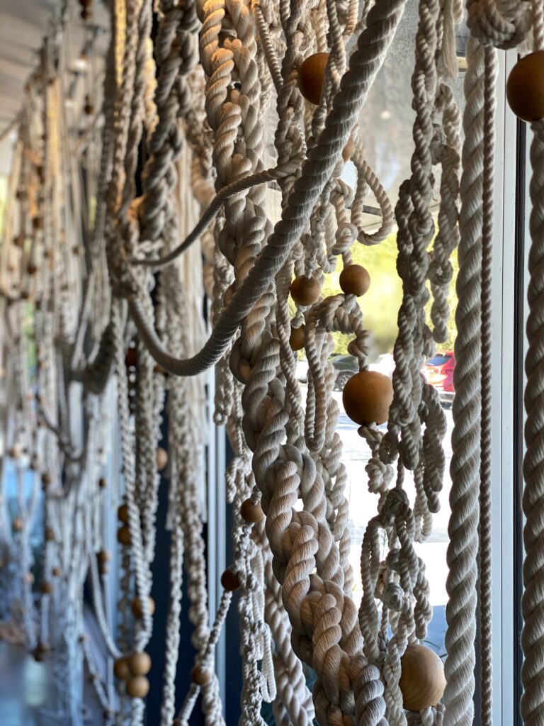 Close-up of the large-scale rope and wood-bead installation at the Ace Hotel in Palm Springs, featuring braided cotton cords cascading along the windows — a sculptural, textural interior design detail.